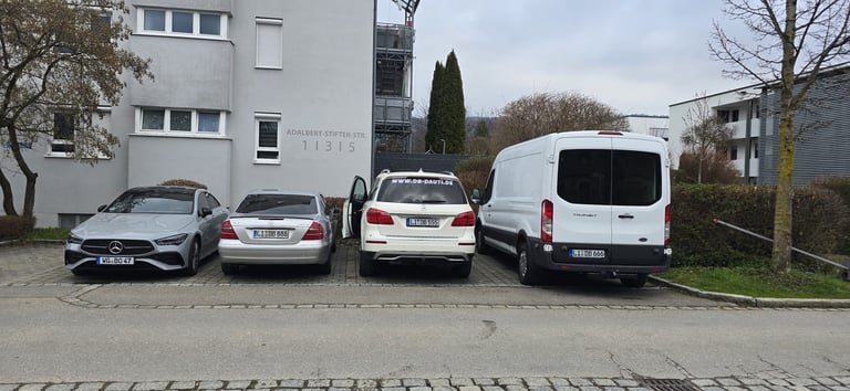 Row of four parked vehicles on a street in front of residential apartment buildings