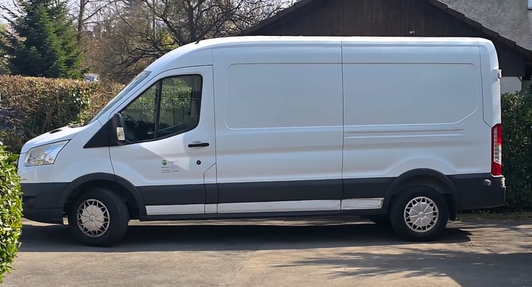 White commercial van parked outside a building with hedges and trees in the background