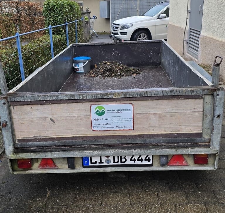 Rear view of a large open utility trailer filled with soil and leaves in a driveway.